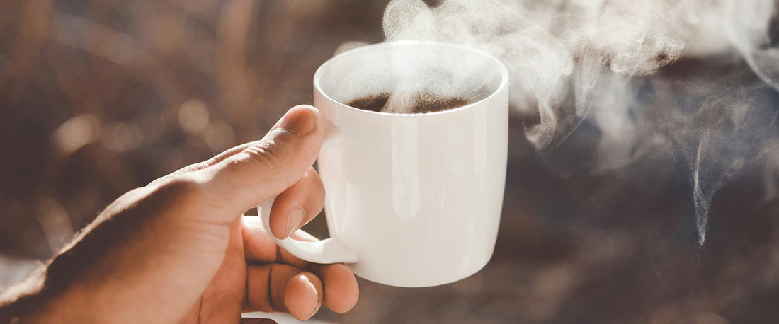 Holding a cup of coffee with steam coming off of it.