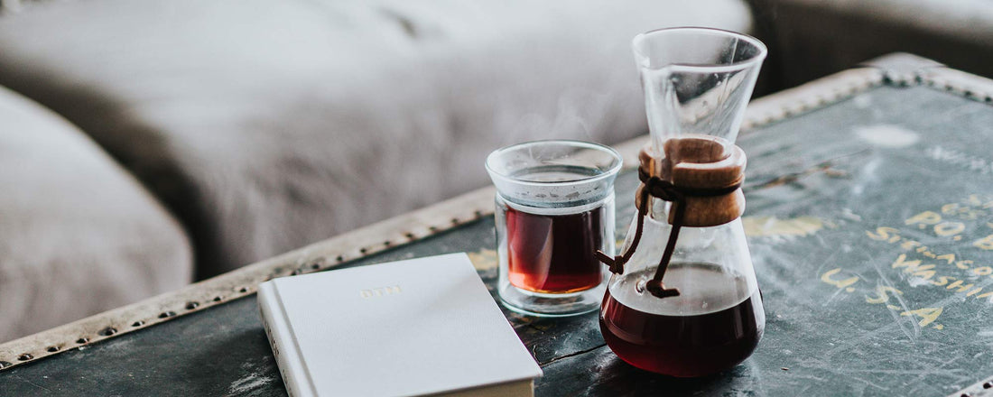 A chemex and clear glass of coffee sitting on top of a coffee table.