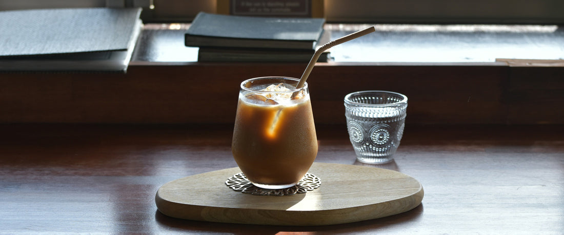 Iced coffee in a window sill with a stack of books. Image Source: Geoff Oliver via Unsplash