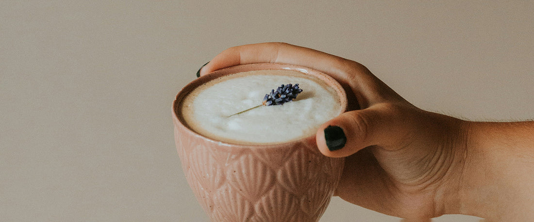 A hand holding a cup of coffee with lavender in it.