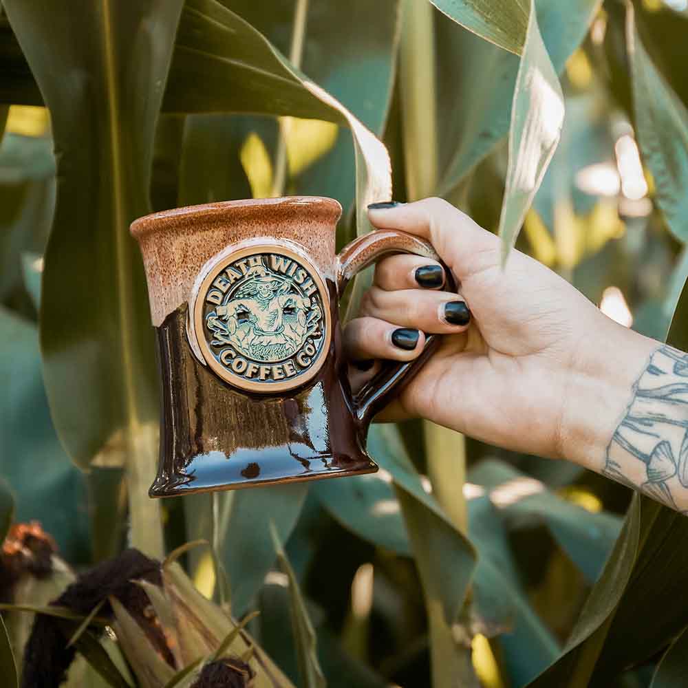 A hand holding the Death Wish Coffee Scarecrow Mug.