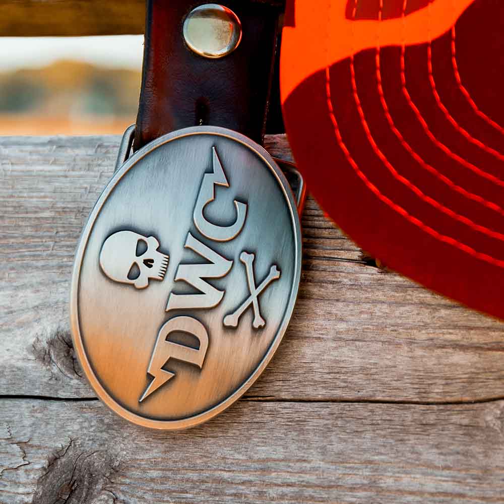 The Death Wish Coffee Bolt Belt Buckle resting on a wooden fence.