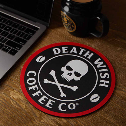 The Death Wish Coffee Bold Logo Mouse Pad on a desk next to a coffee mug.